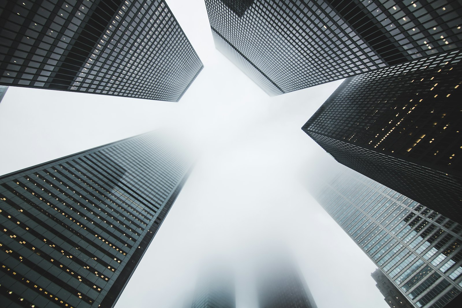 Looking straight up between four glass towers converging on an open square of sky