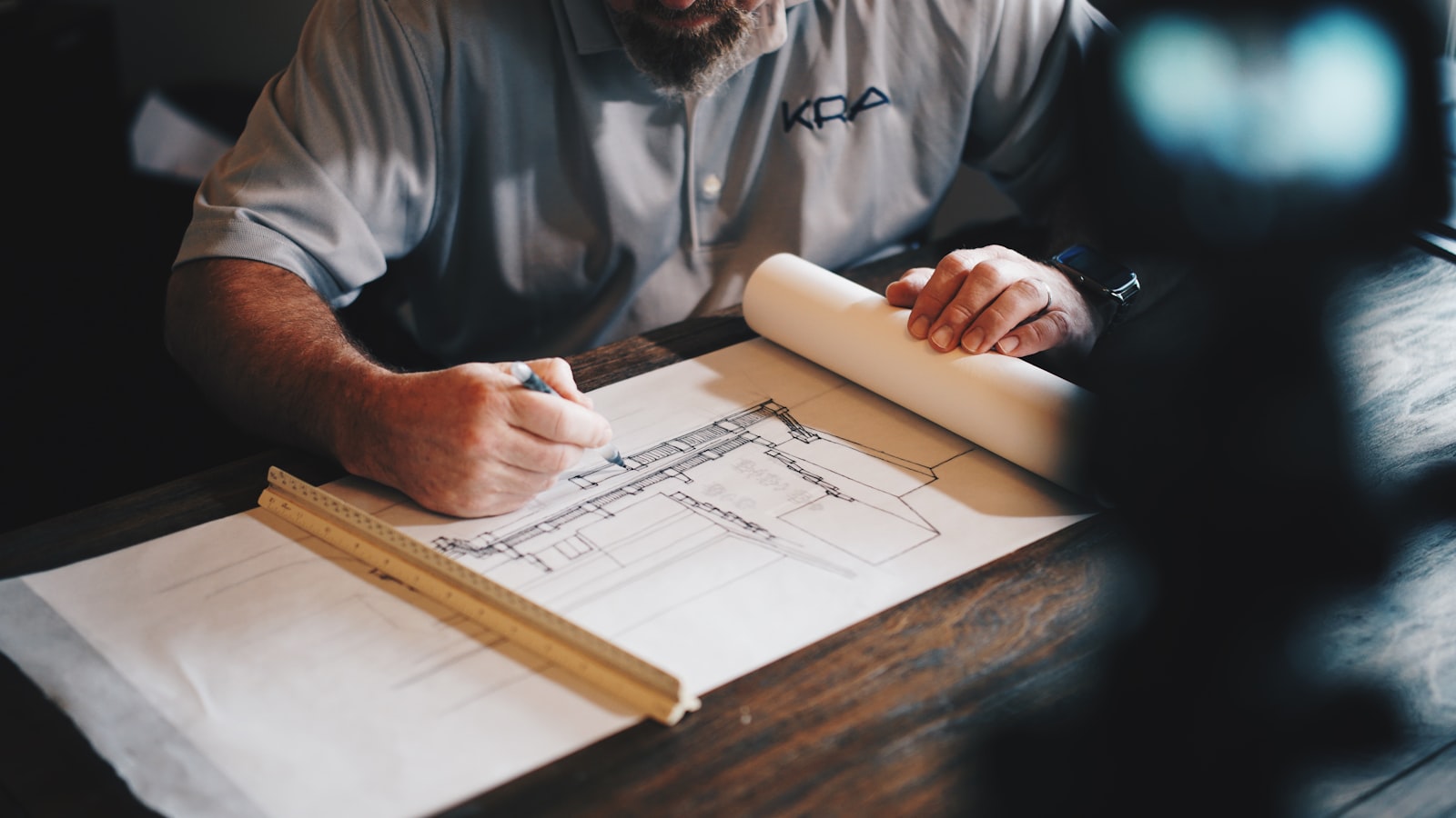 Architect drafting a detail by hand in pencil at a warm wooden desk